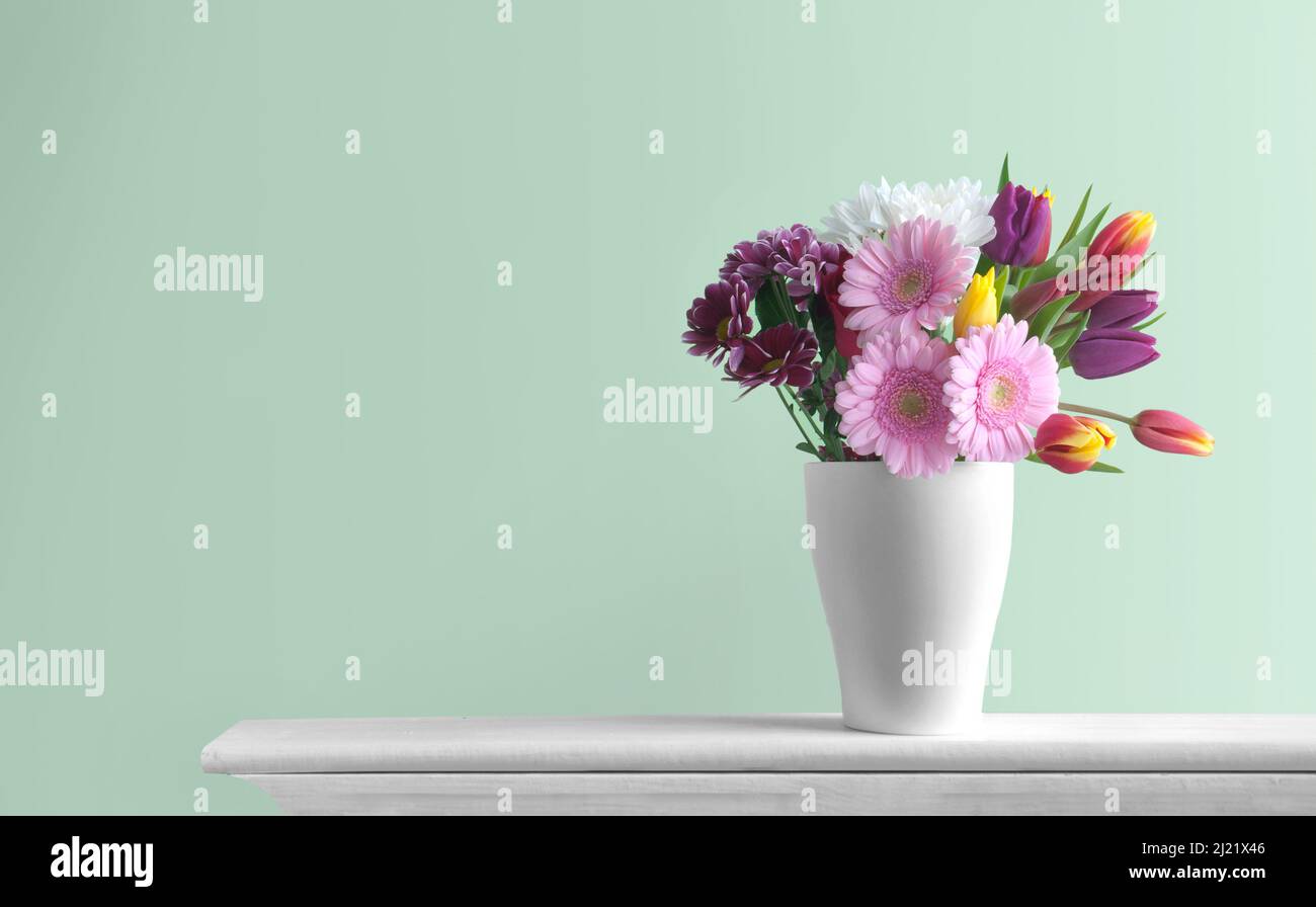 Selection of spring flowers inside a pot on top of a fireplace mantelpiece Stock Photo