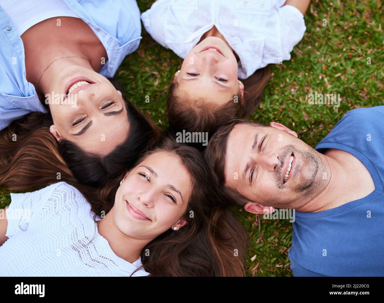 Were just a bunch of peas in a pod. Portrait of a cheerful family lying on the ground together outside in a park during the day. Stock Photo