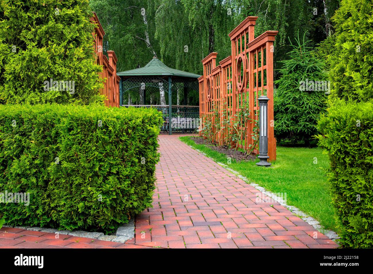 Vertical pergola made of brown wood in a roses garden with a stone tile walkway with granite curb and ground lantern in backyard in a garden with plan Stock Photo