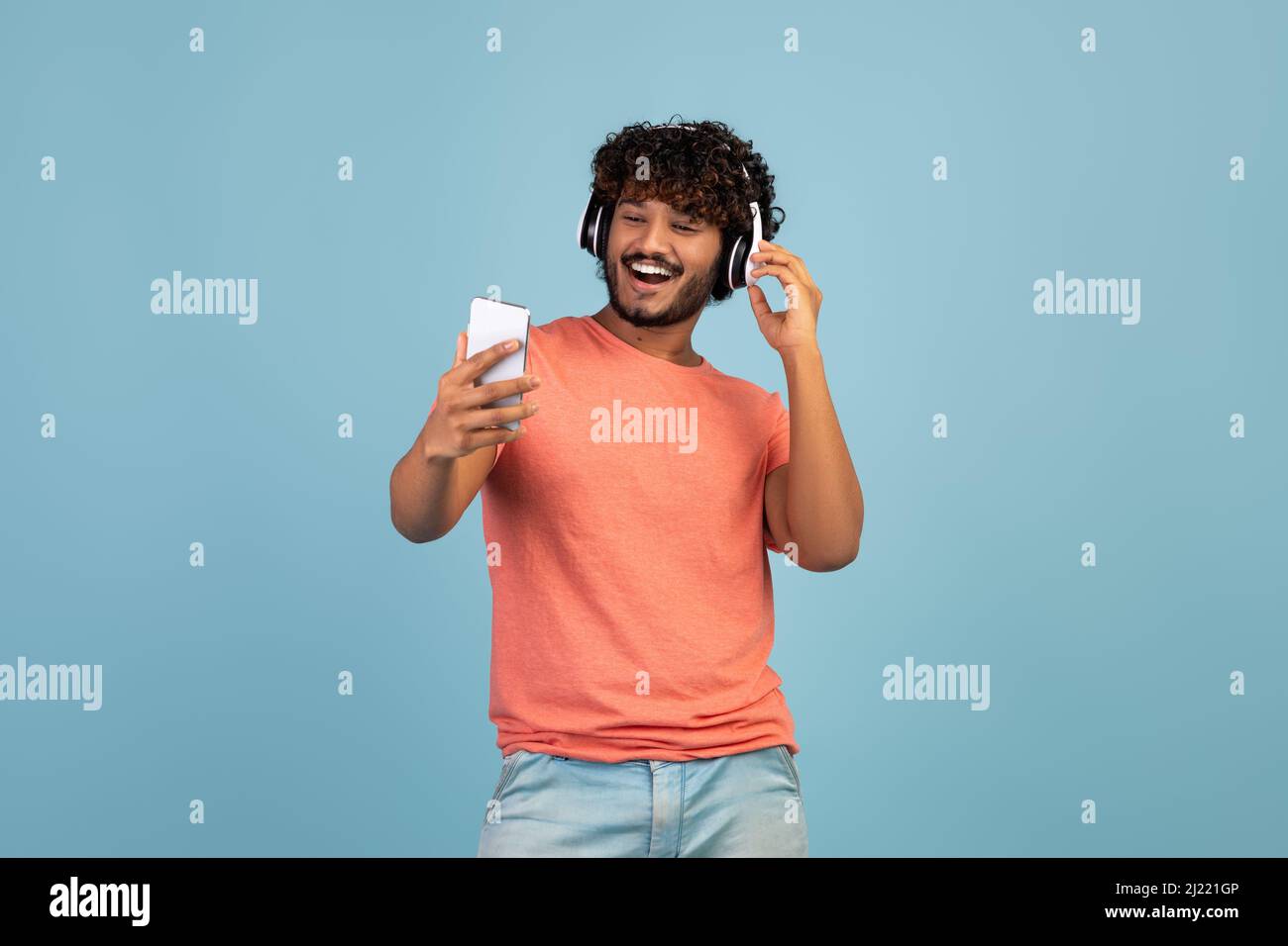 Excited eastern guy using wireless headset and smartphone, copy space Stock Photo