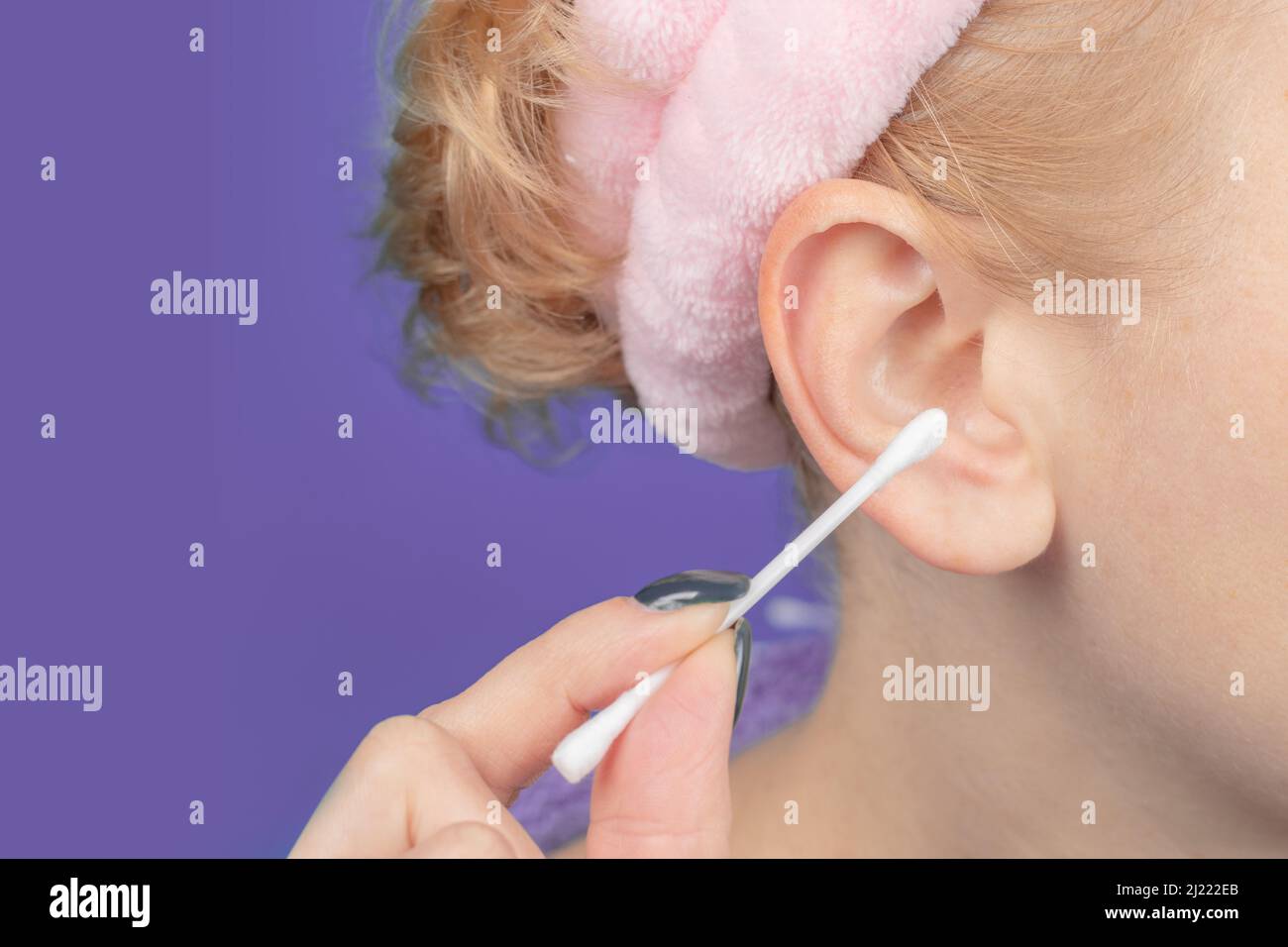 Female cleaning ear with cotton bud on violet background Stock Photo