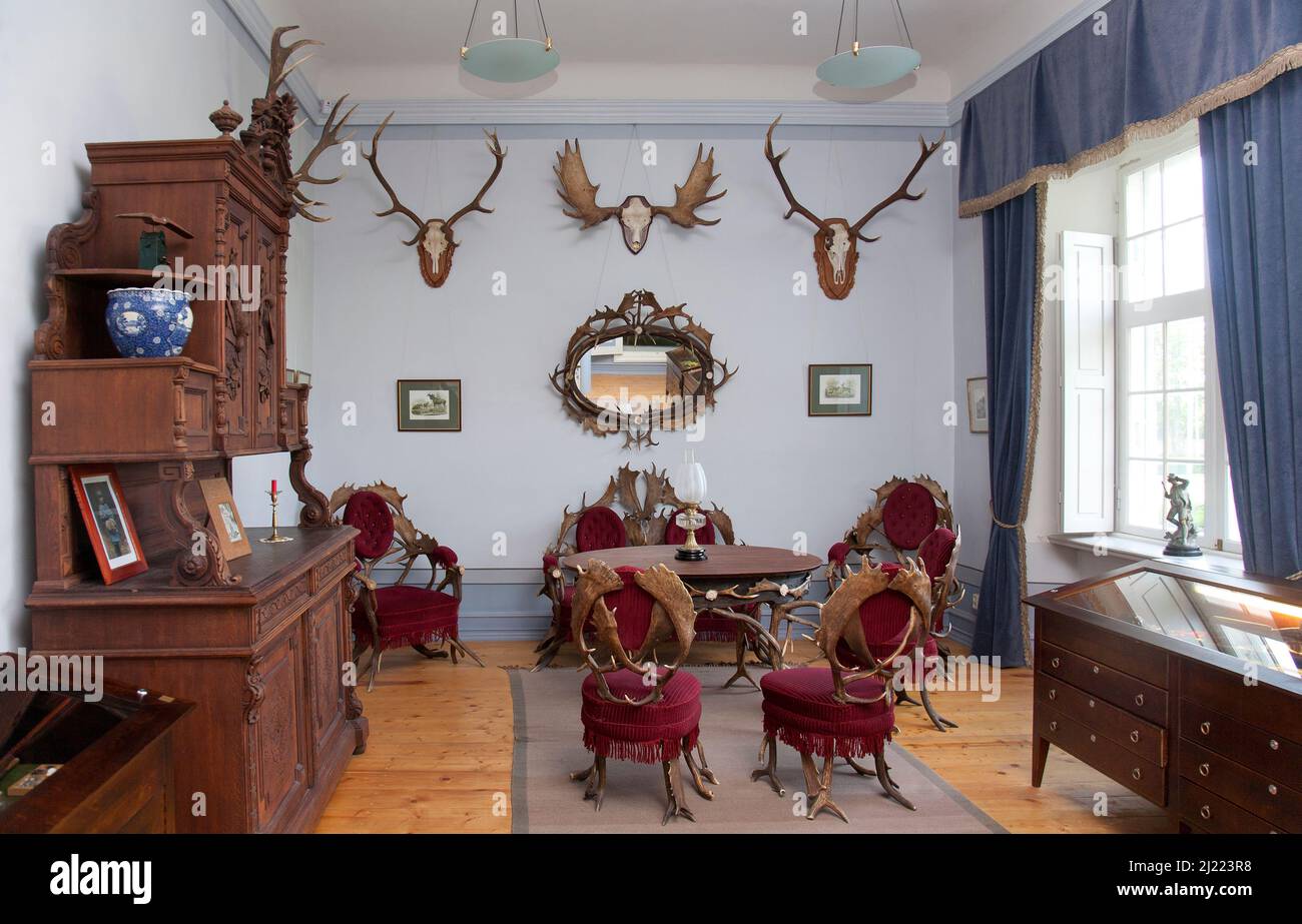 Traditional furniture and hunting trophies, carved chest of drawers, wall plaques and chairs and table made from deer antlers. Stock Photo