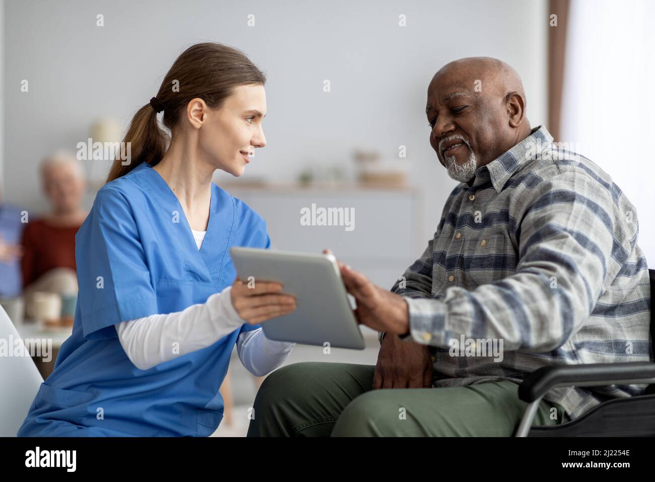 Friendly nurse helping black senior man using digital tablet Stock Photo