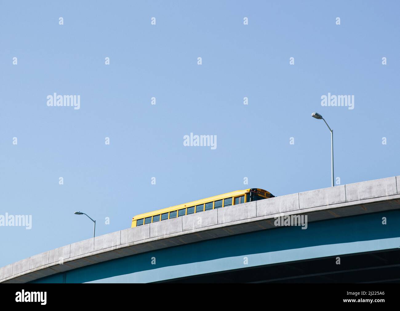 A yellow schoolbus driving over an elevated roadway against a blue sky. Stock Photo
