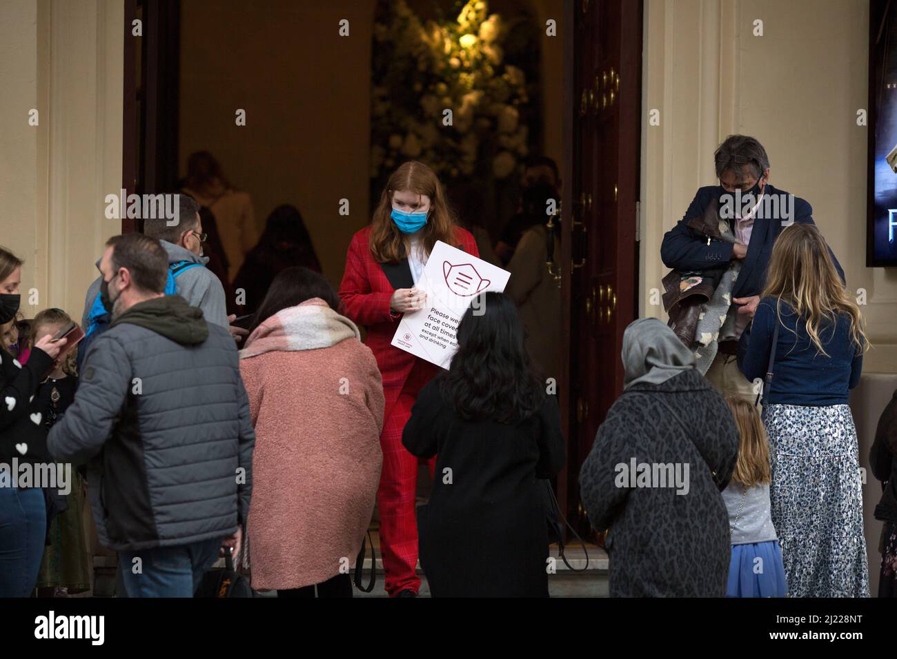 A member of the staff holds a mask-wearing instruction board at Theatre Royal Drury Lane in London after the relaxation of Covid-19 Plan B rules. Stock Photo