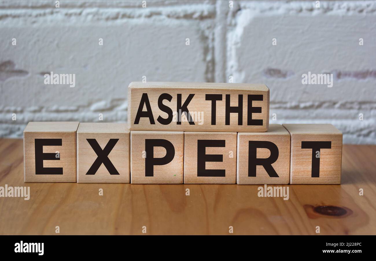 ASK THE EXPERT written on wooden blocks against a white brick wall Stock Photo