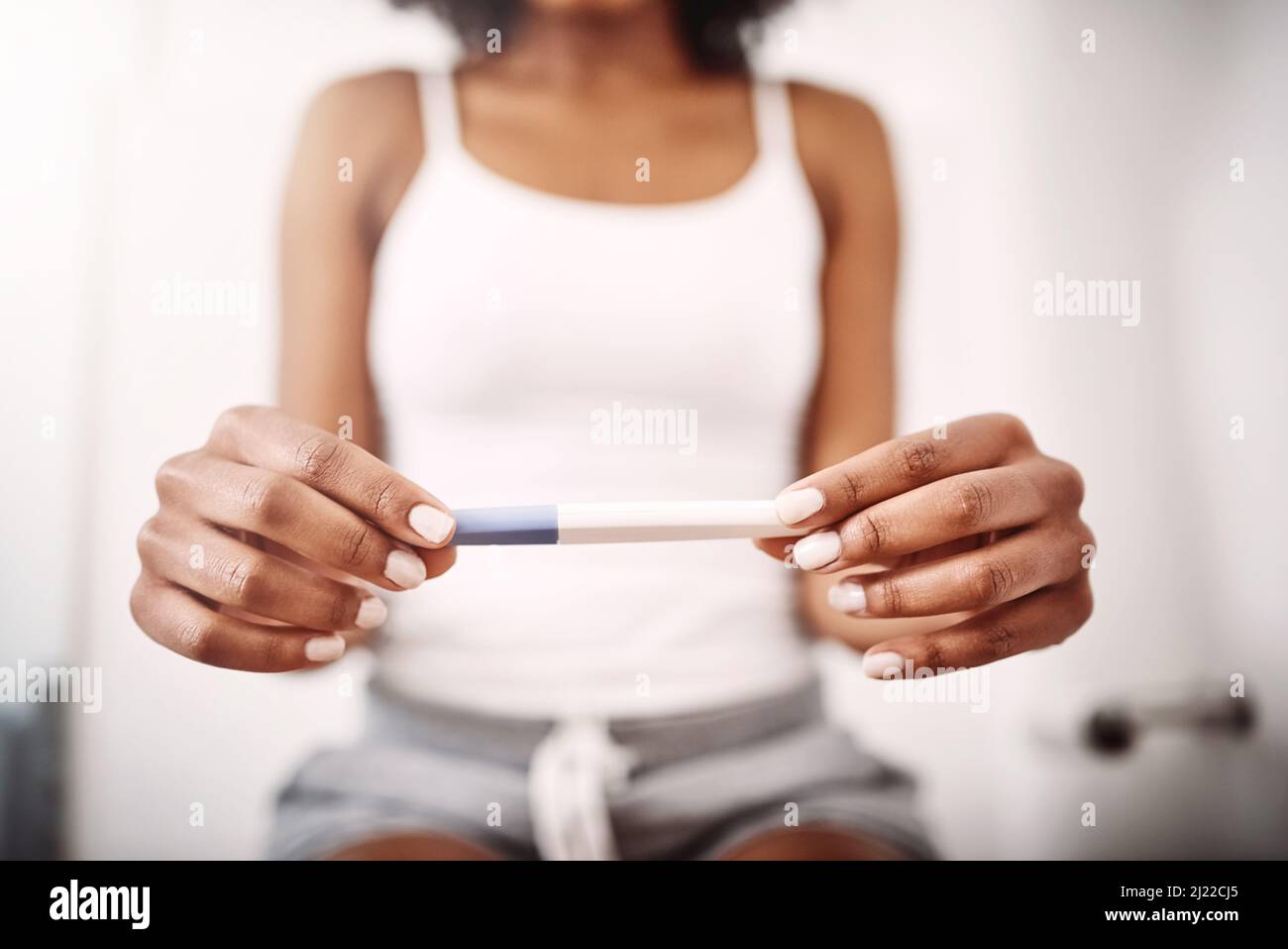 Is it too early to start coming up with names. Shot of an unrecognizable woman holding a pregnancy test stick while sitting on the toilet. Stock Photo