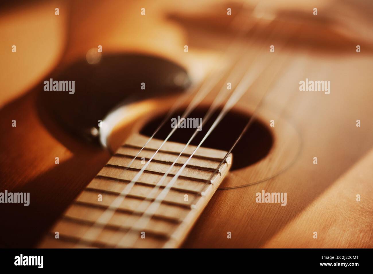An old vintage acoustic guitar with metal strings is illuminated by sunlight. A musical instrument. Solfeggio. Stock Photo