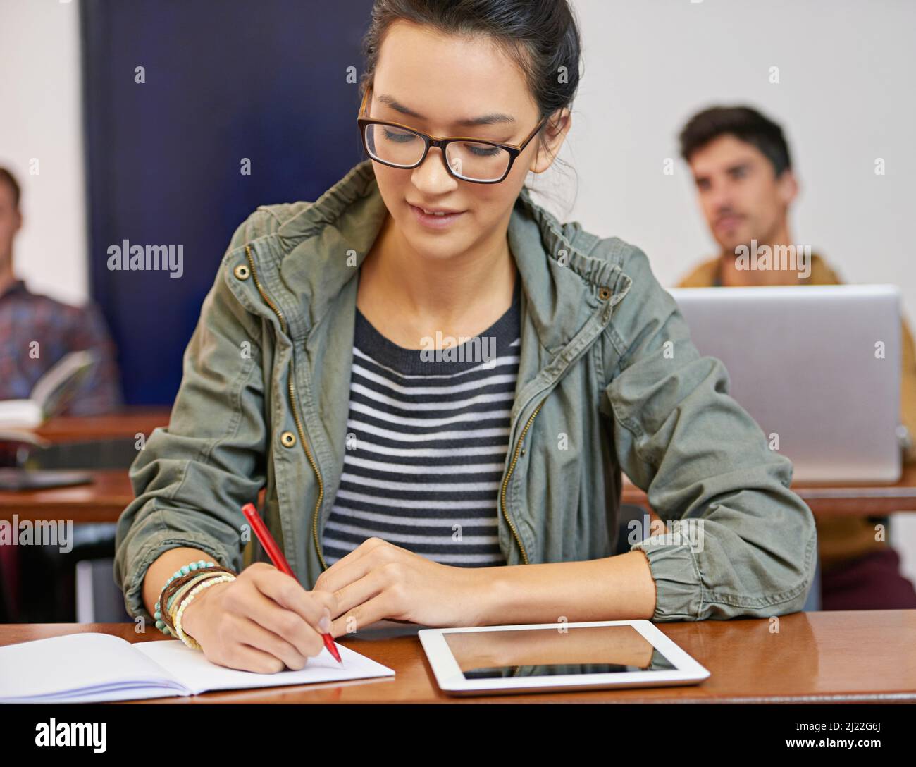 Doing the work to achieve her dreams. Cropped shot of a young woman using notes and digital tablet in class. Stock Photo