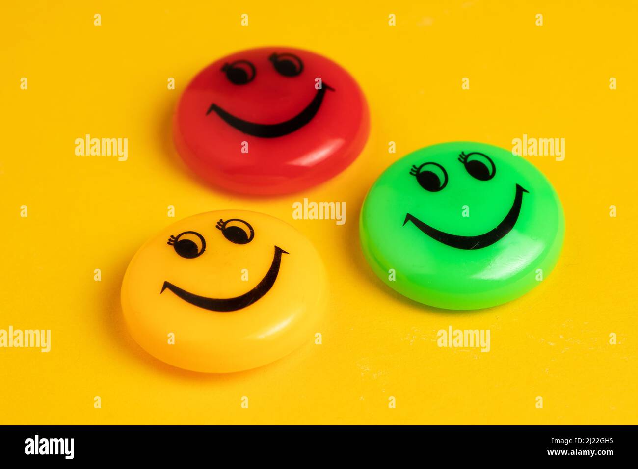 Green yellow and red round magnet with smile in a row on a yellow ...