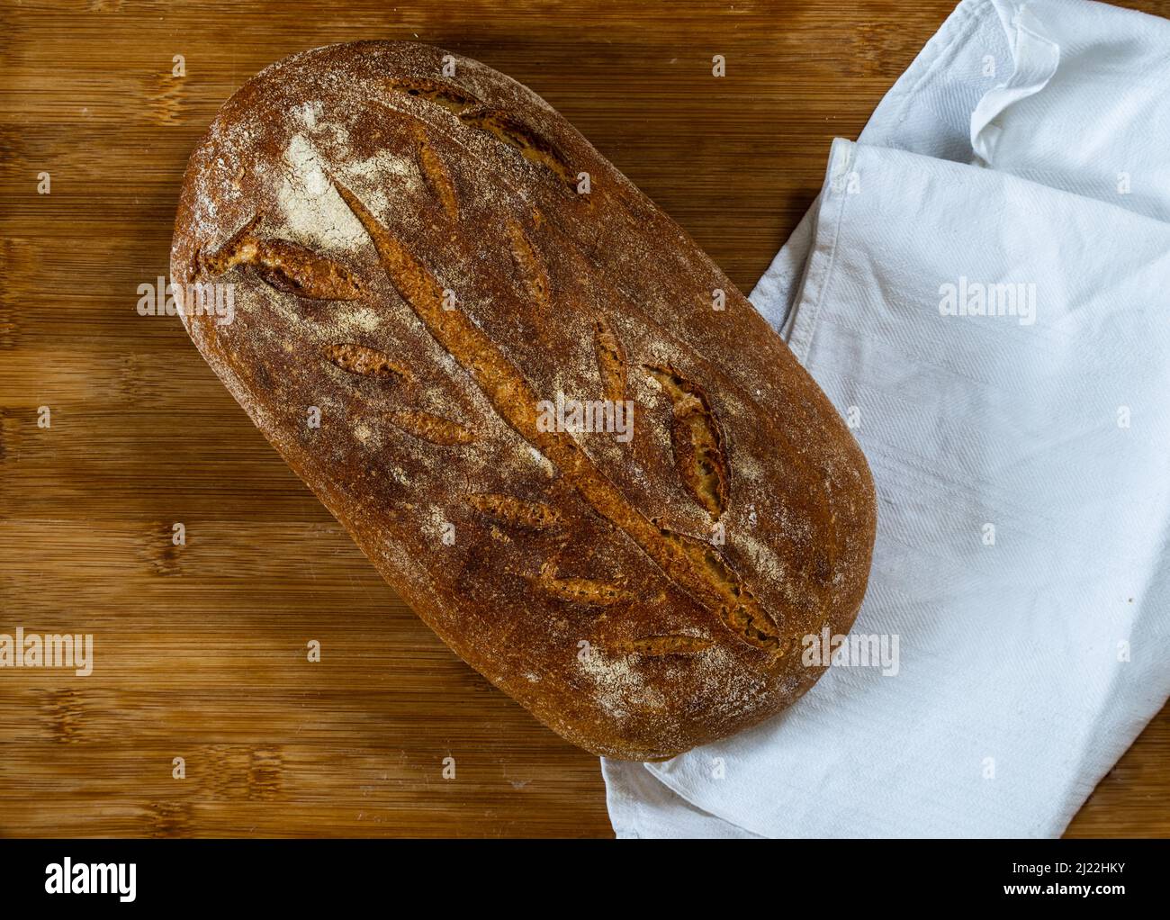 whole grain wheat bread made with sour dough on wooden surface with white cloth shot from above