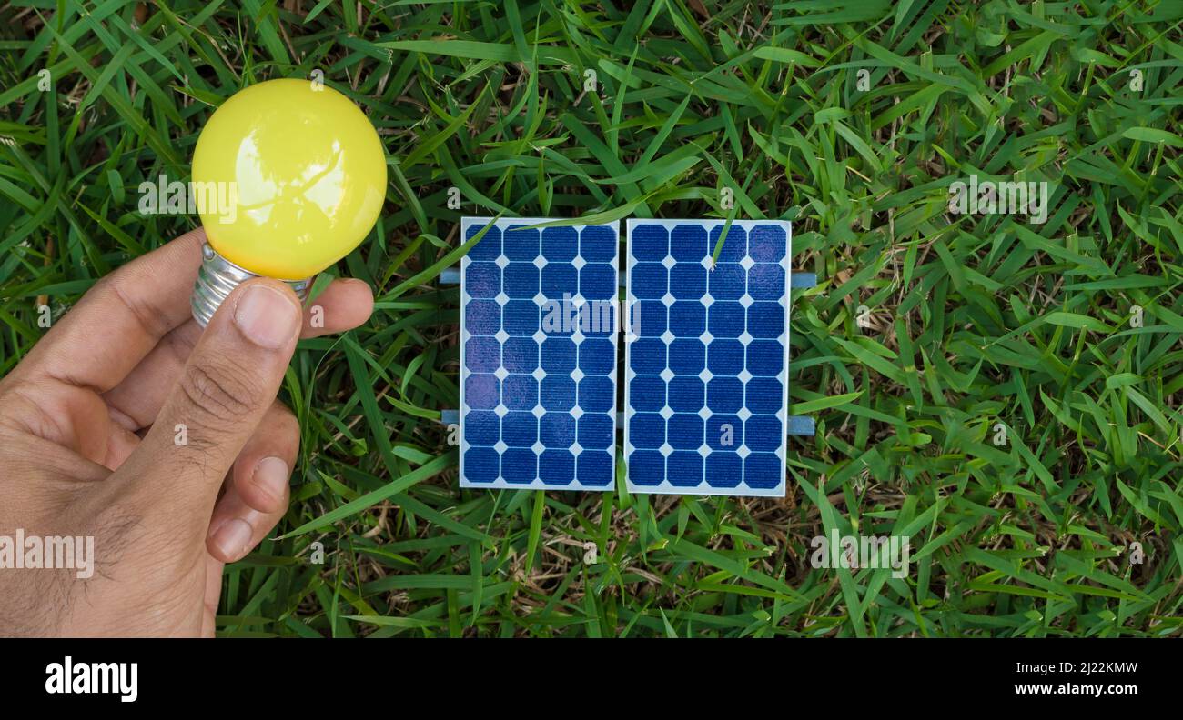 Holding a lamp next to a photovoltaic solar panel on grass background ...