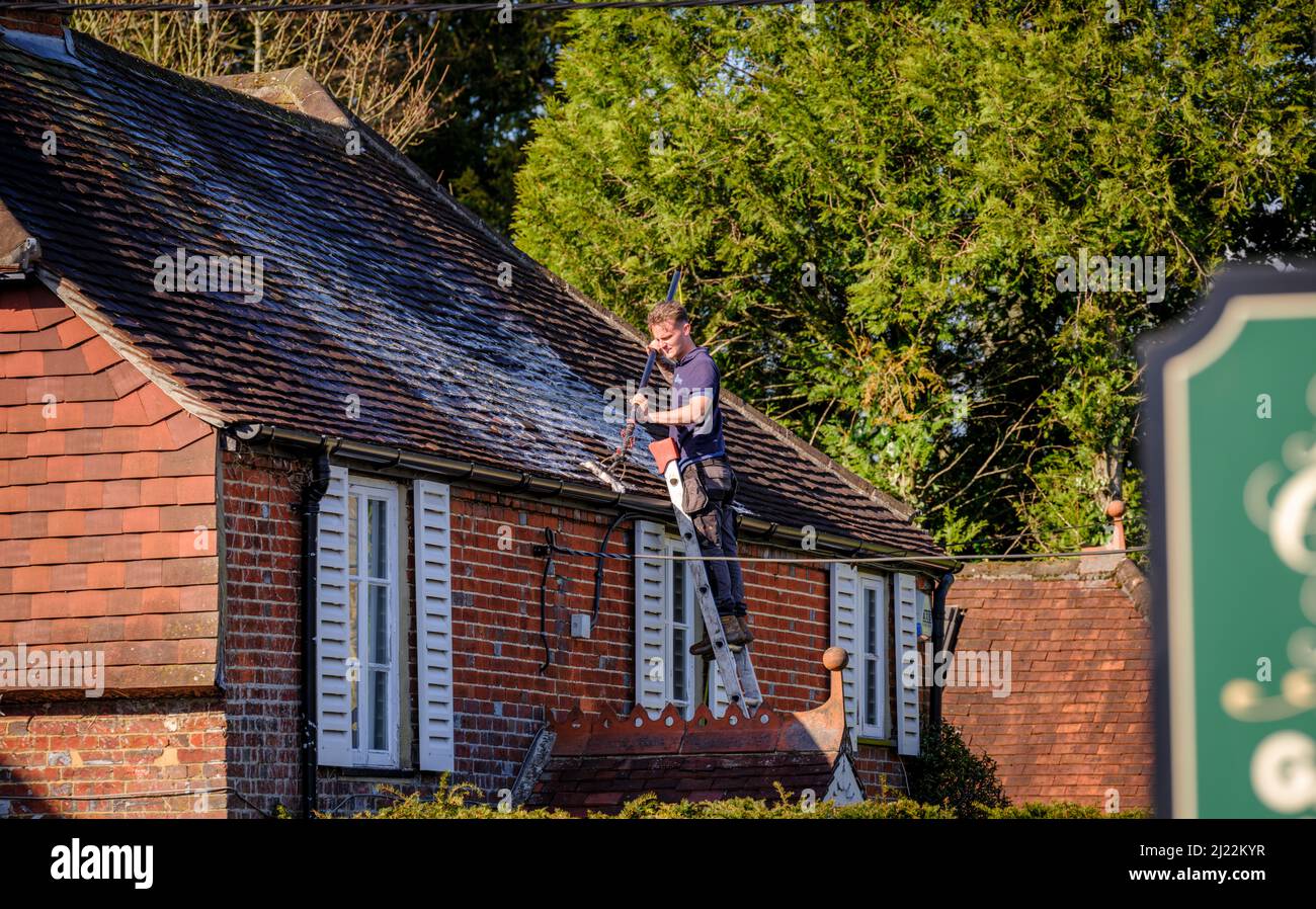 Exton, Hampshire - a tradesman up ladder cleaning moss from roof tiles on one of the houses in the centre of the village. Editorial Use Only Stock Photo