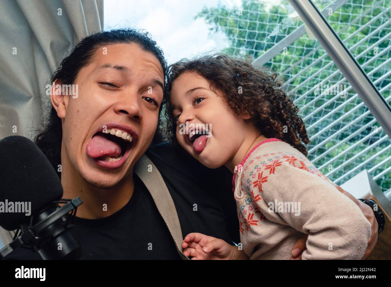 Venezuelan Caucasian father and daughter singing and making funny and crazy faces, man and girl having fun indoors. Stock Photo
