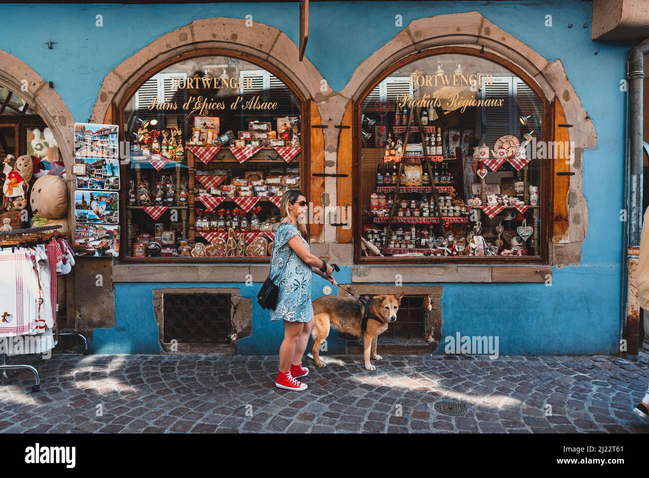 A female with her dog standing on the street against a grocery boutique in Colma, France Stock Photo
