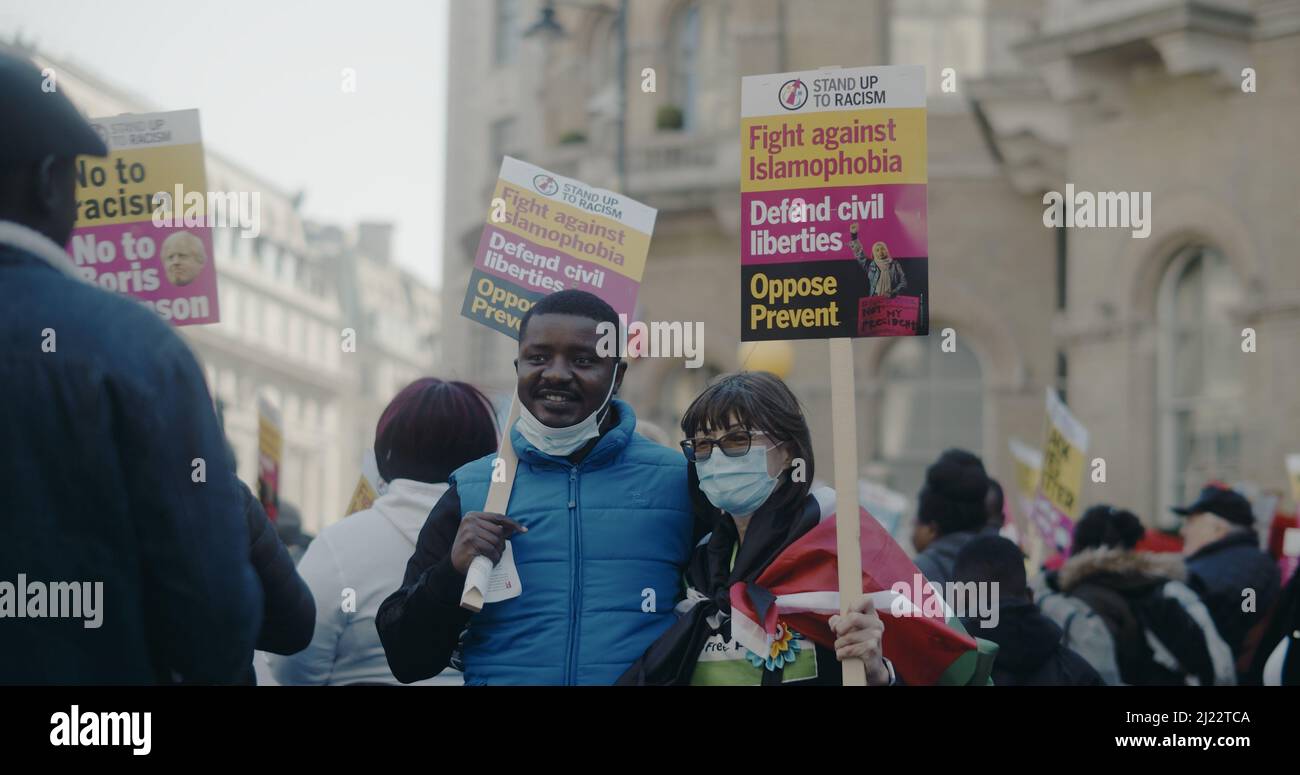 London, UK - 03 19 2022:  Black man and woman holding signs whilst having photo taken, ‘Stand Up To Racism…’, at Portland Place. Stock Photo