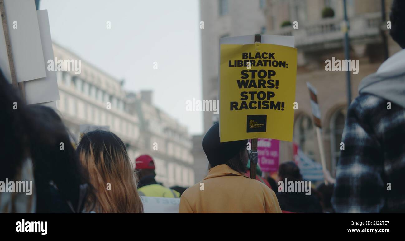 London, UK - 03 19 2022:  Woman protester in crowd holding a sign at Portland Place, ‘Black Liberation:  Stop Wars!  Stop Racism!’. Stock Photo