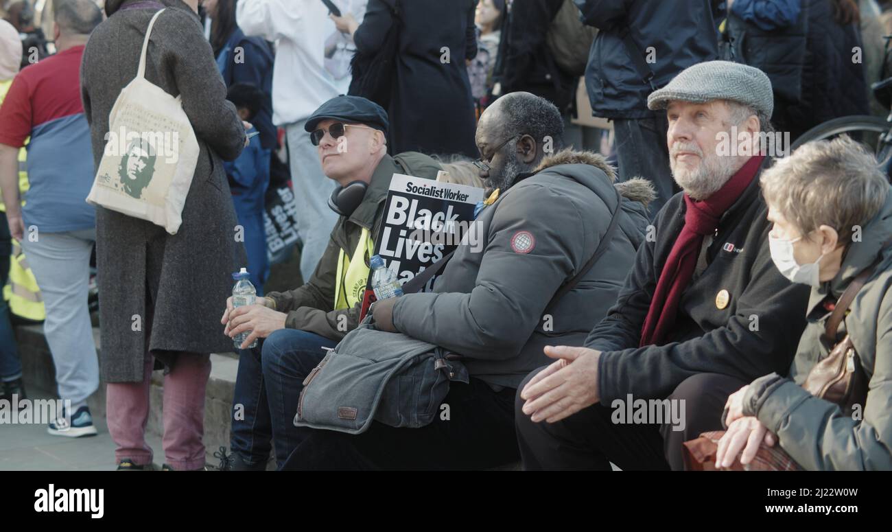 London, UK - 03 19 2022:  A black man protester sitting at Parliament Square holding a sign, Black Lives Matter’, for the yearly ‘March Against Racism'. Stock Photo