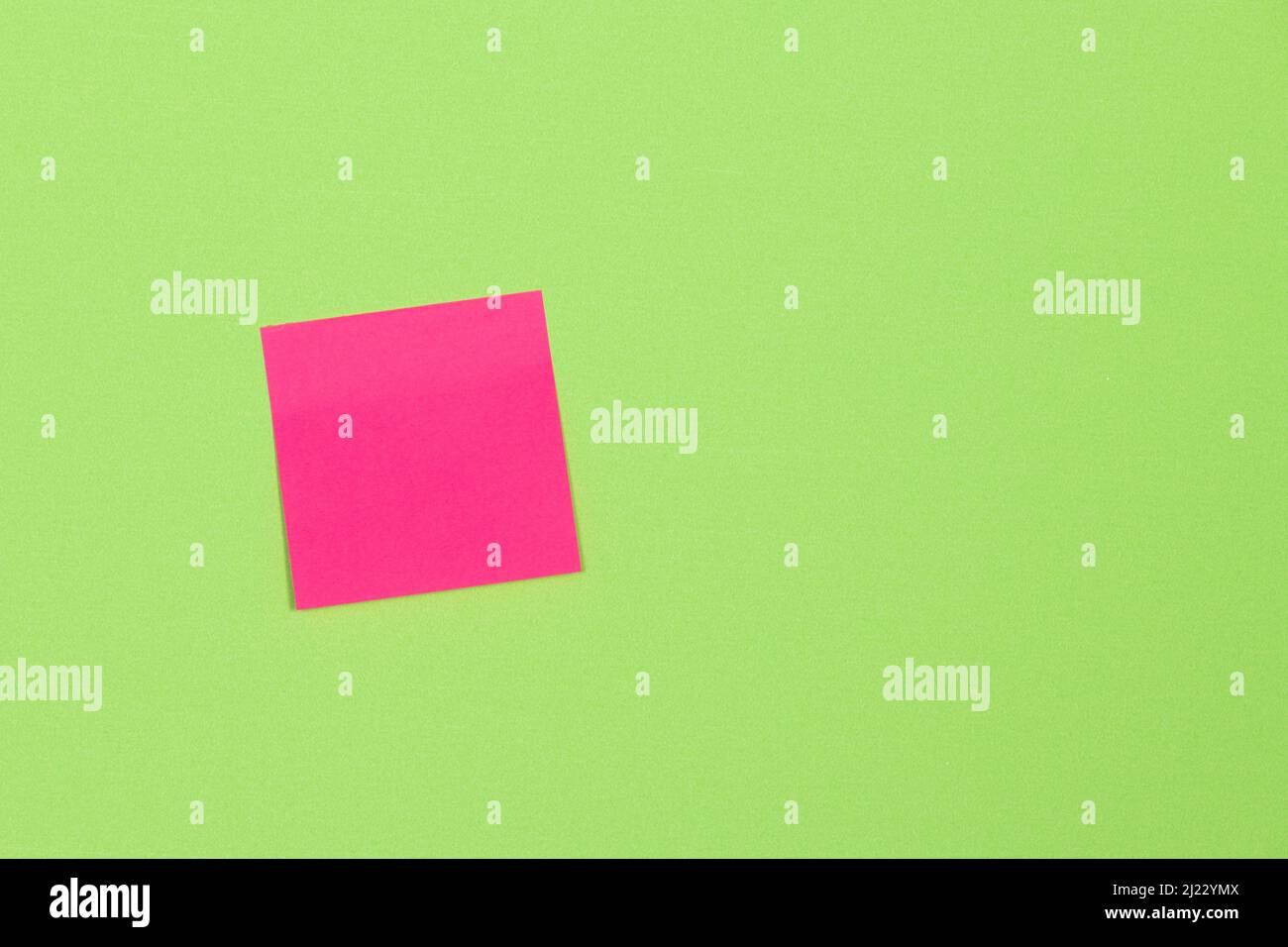 blank pink adhesive note stuck to a green background. Stock Photo