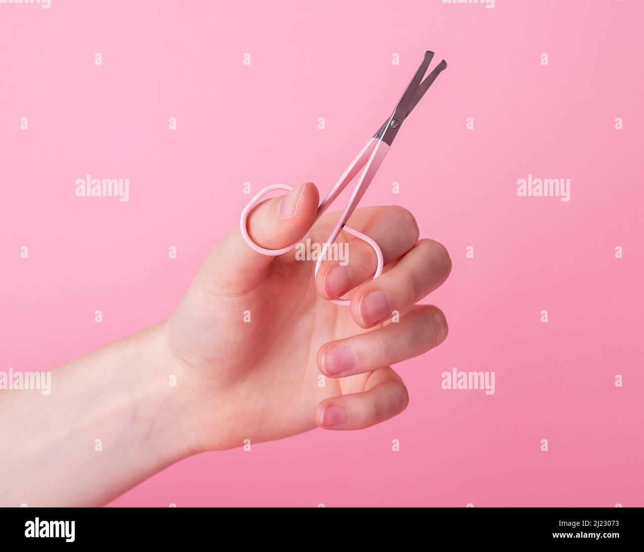Woman hand holding nail scissors for manicure on pink background. Tool for beauty procedure. Hygiene and care concept. High quality photo Stock Photo