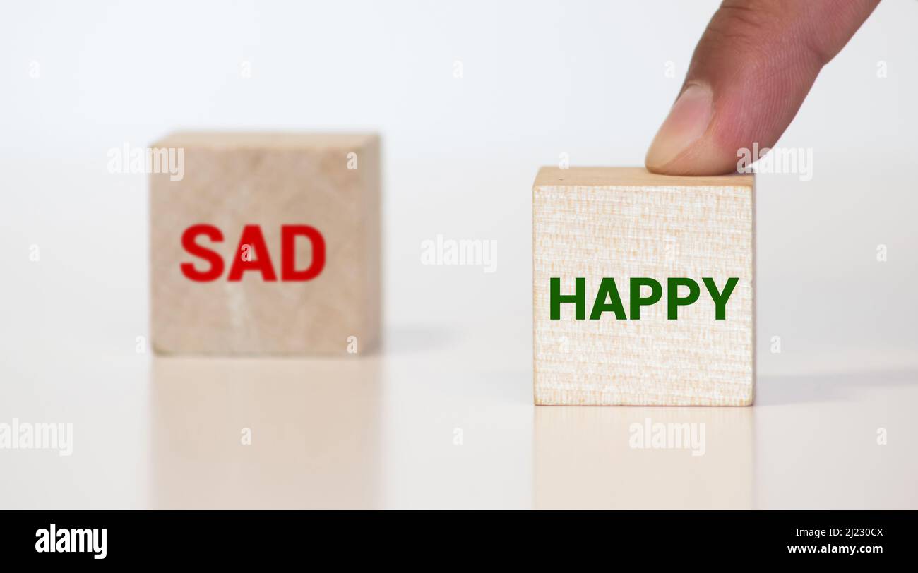 Positive and negative emotions. Positive and negative thinking. Smiling and sad emoticons on wooden cubes on a white and black background. Stock Photo