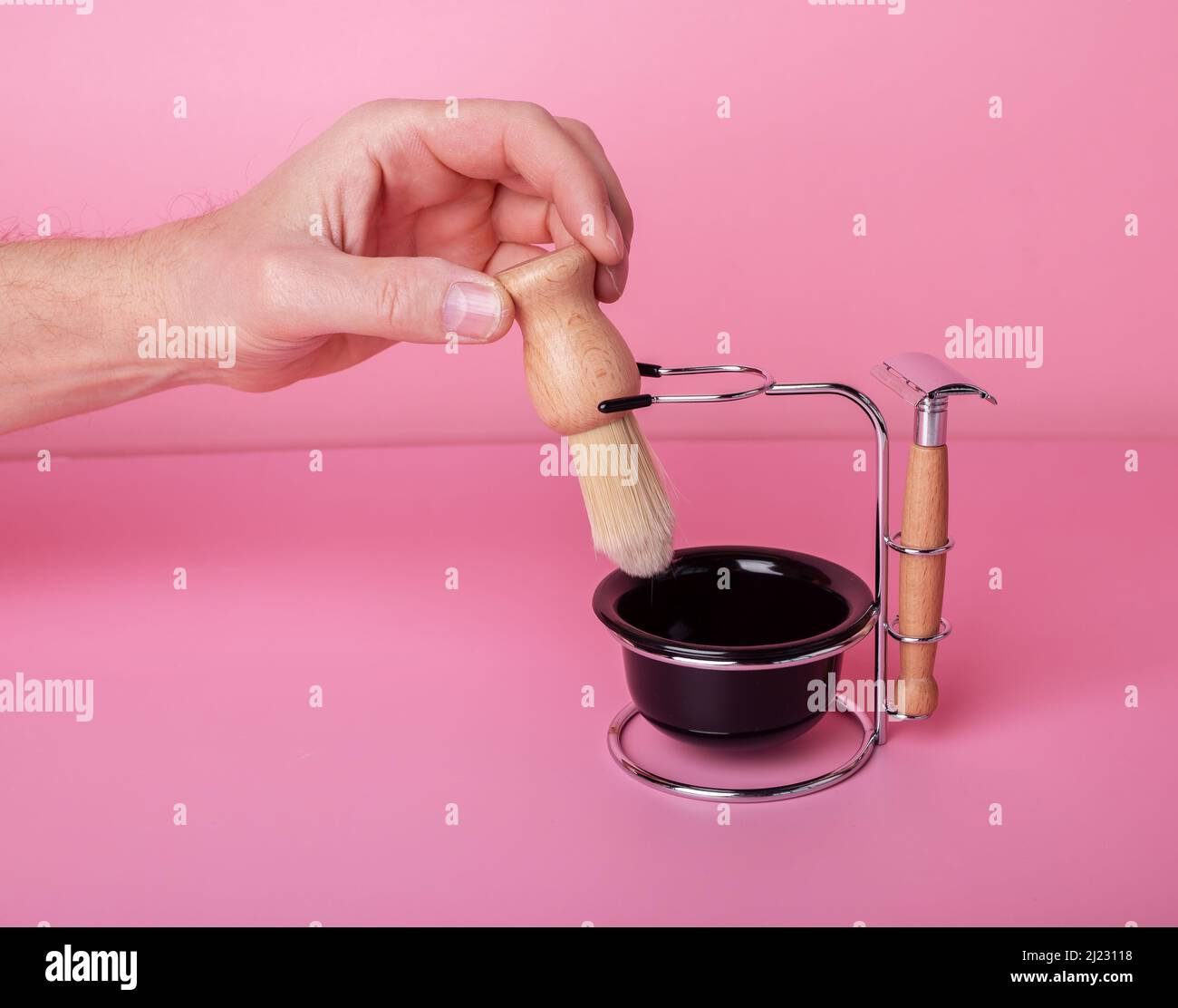 Man hand holding shaving brush. Grooming set, razor, cup for foam on pink background. Hygiene and face care concept. High quality photo Stock Photo