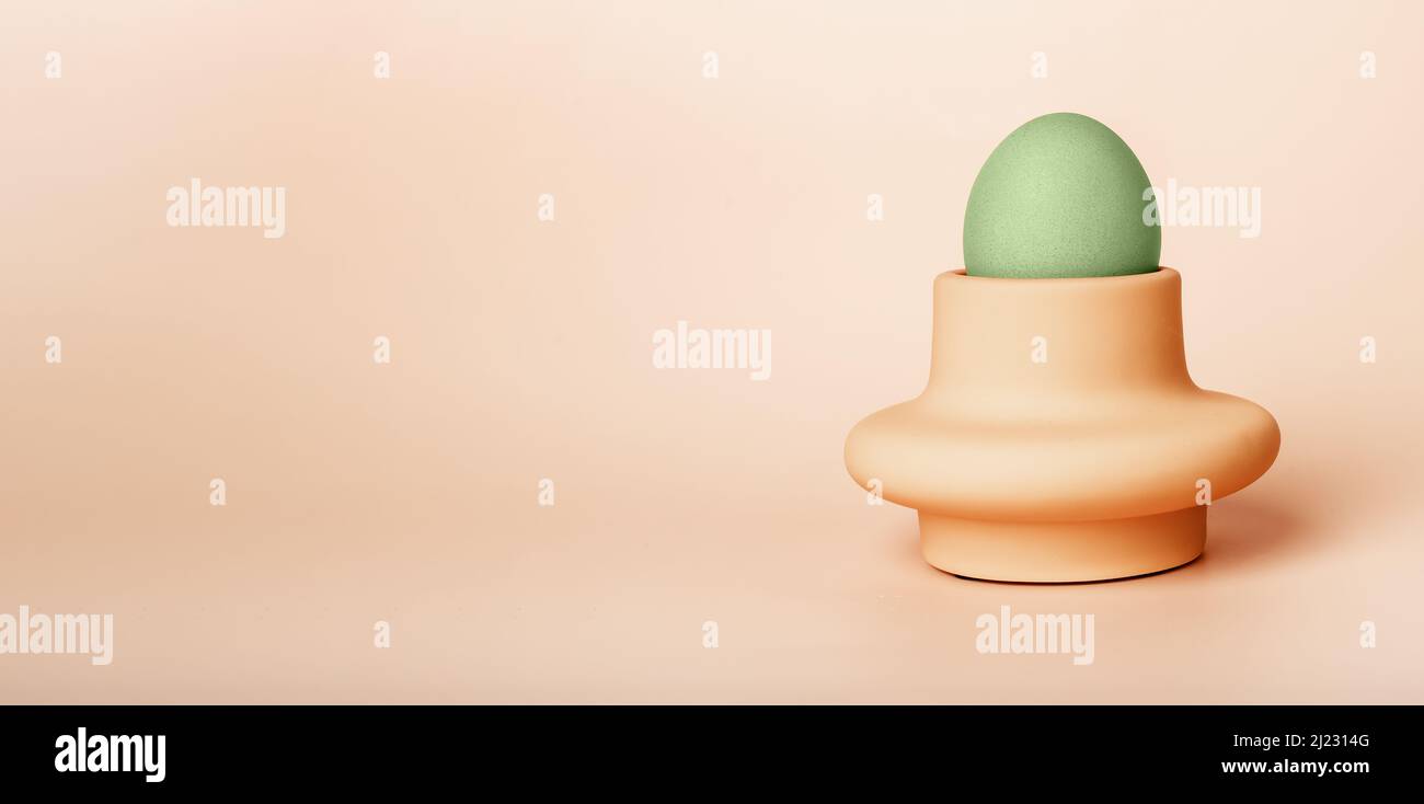 Banner with green dyed Easter egg in cup, server or holder on beige background. Religious holiday symbol. Breakfast food. Space for text. High quality photo Stock Photo
