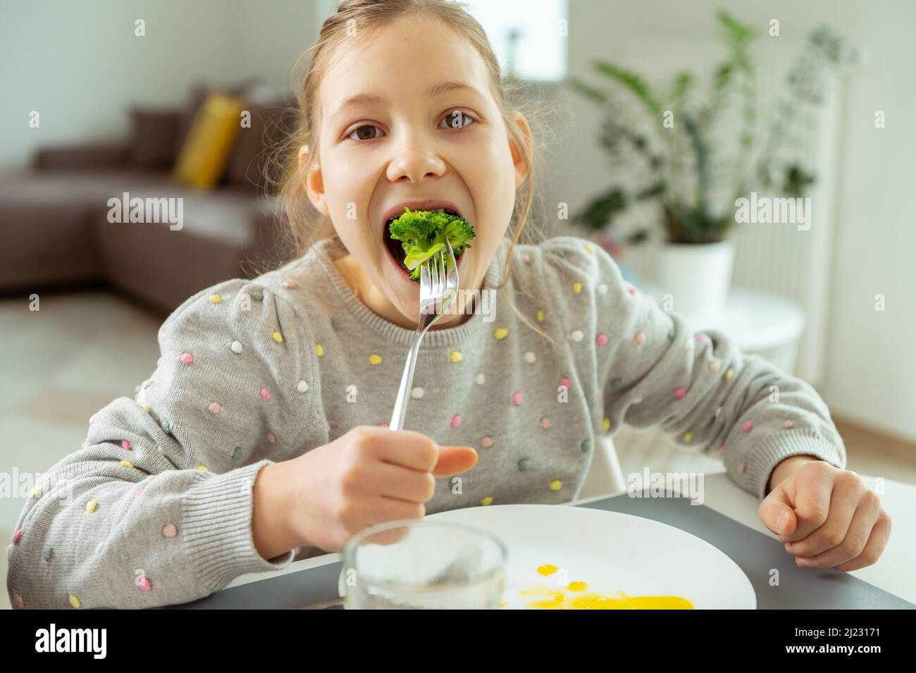 Cute teen girl eating green fresh broccoli during her lunch Stock Photo