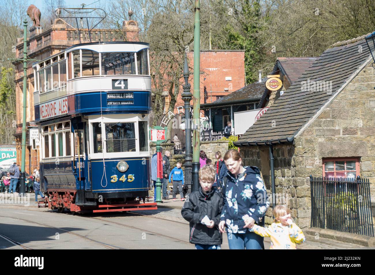Derbyshire, UK – 5 April 2018: Family crossing the track before the 345 double decker vintage tram at the Red Lion tram stop, Crich Tramway Village Stock Photo