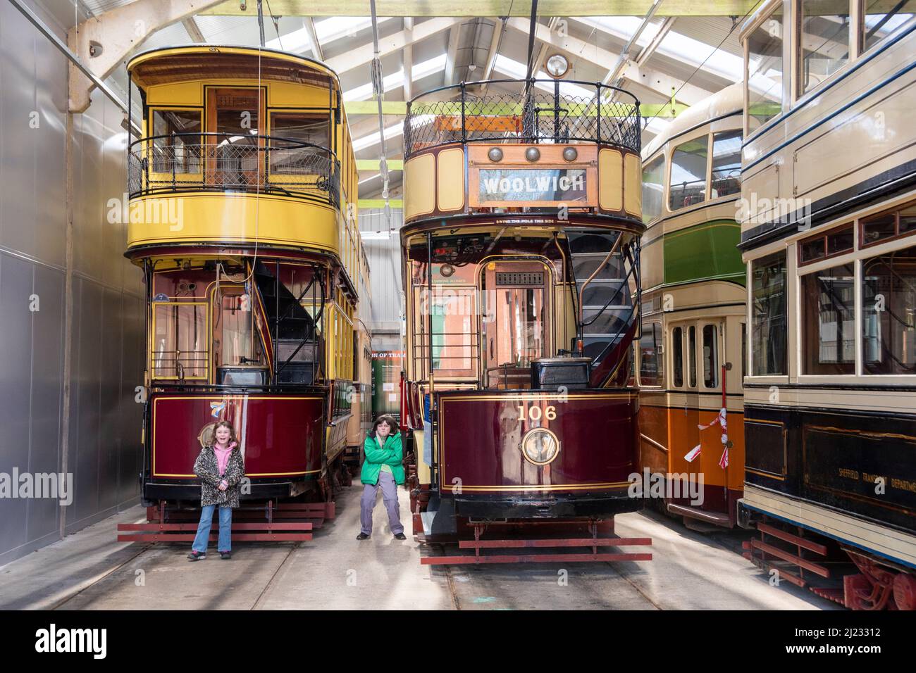 Derbyshire, UK – 5 April 2018: Two children pose before the vintage trams stored in the vehicle garage at Crich Tramway Village Stock Photo