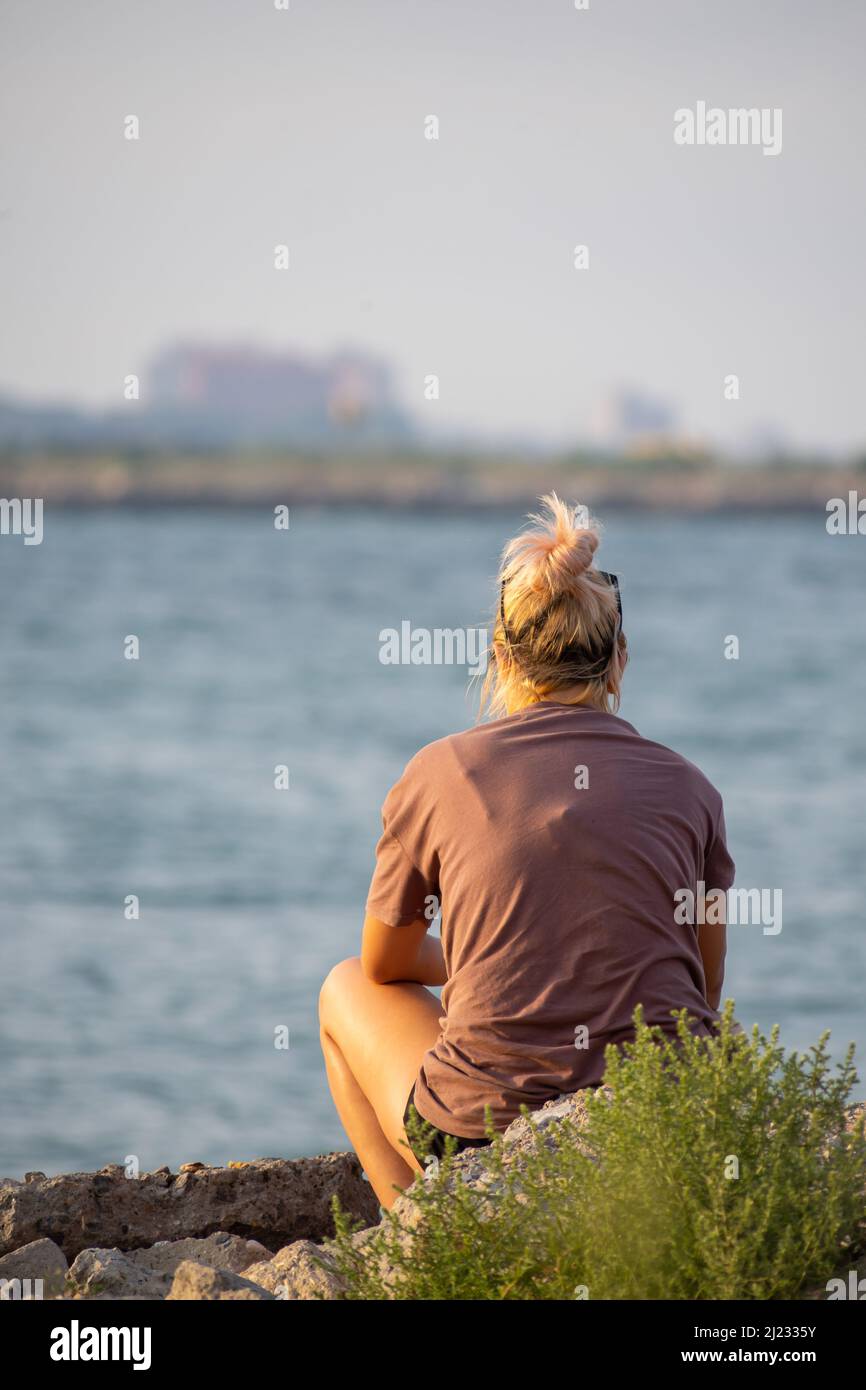 Woman sitting on a rock and tying to cath fish. Unrecognisable person. Stock Photo