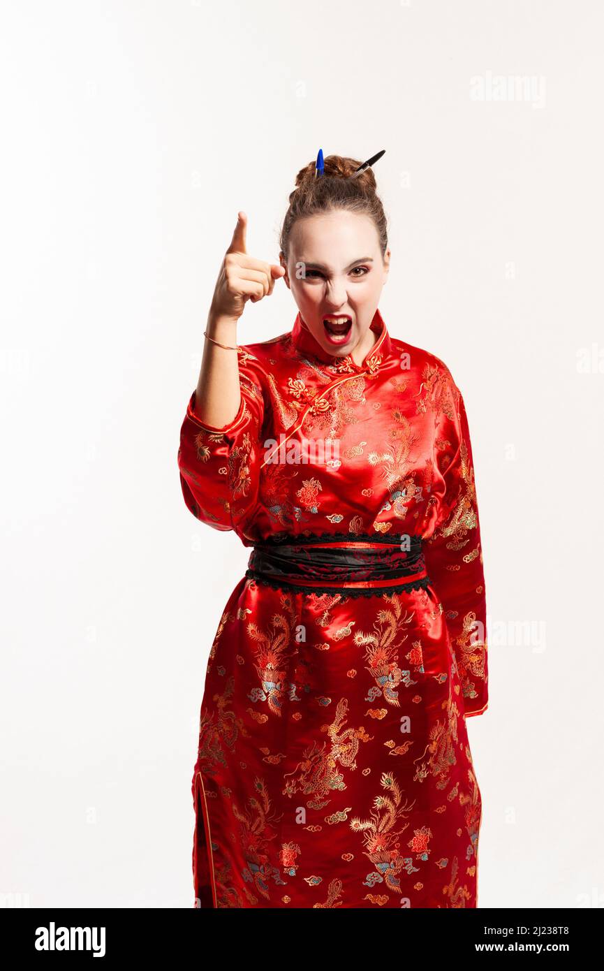 young man in red oriental costume, looking directly at the camera, shouting and raising his arm in a threatening and reprimanding gesture with his fin Stock Photo