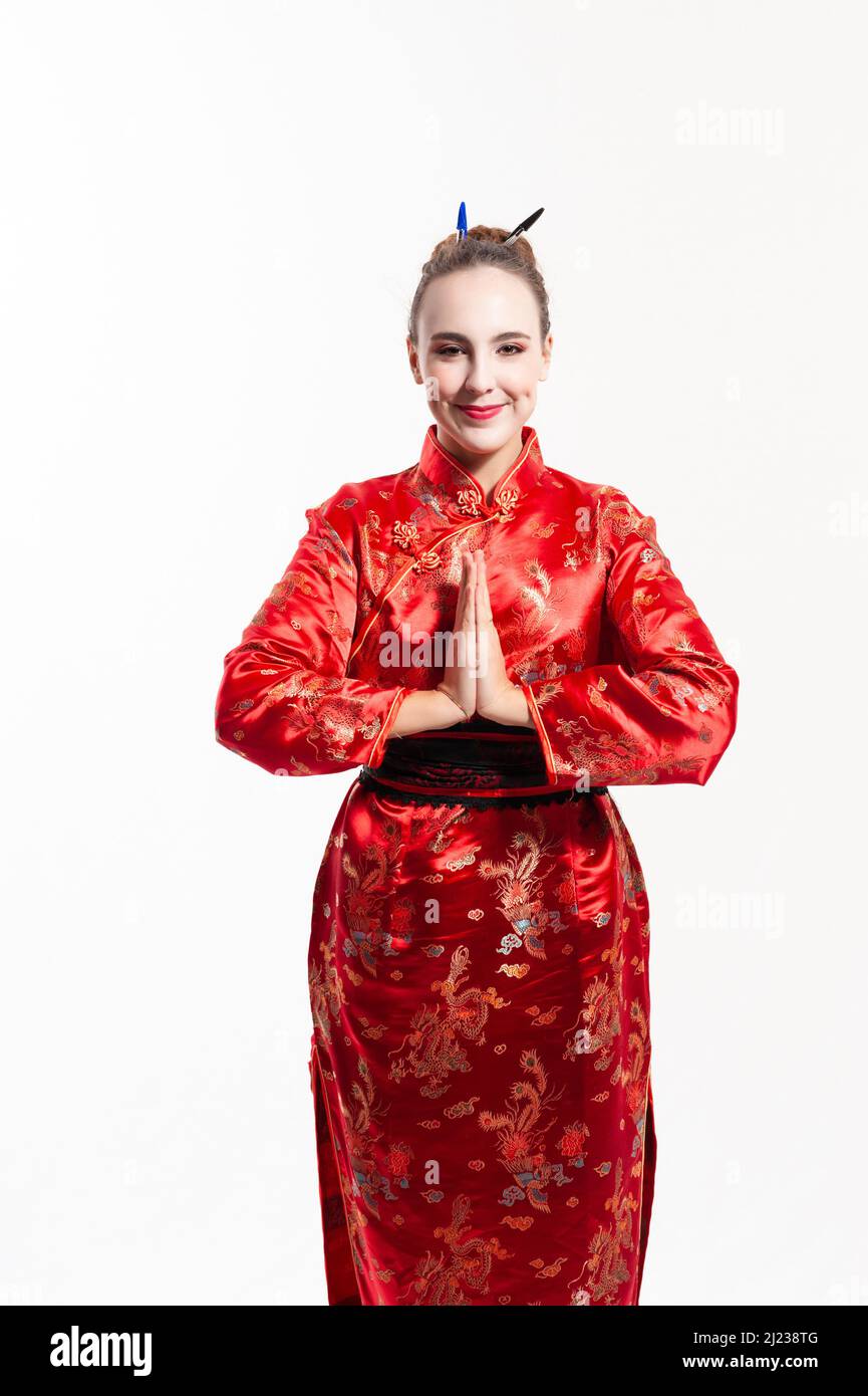 young woman dressed in a traditional red Chinese costume, with white make-up , with a bun in her hair held in place by pens, smiling and making the tr Stock Photo