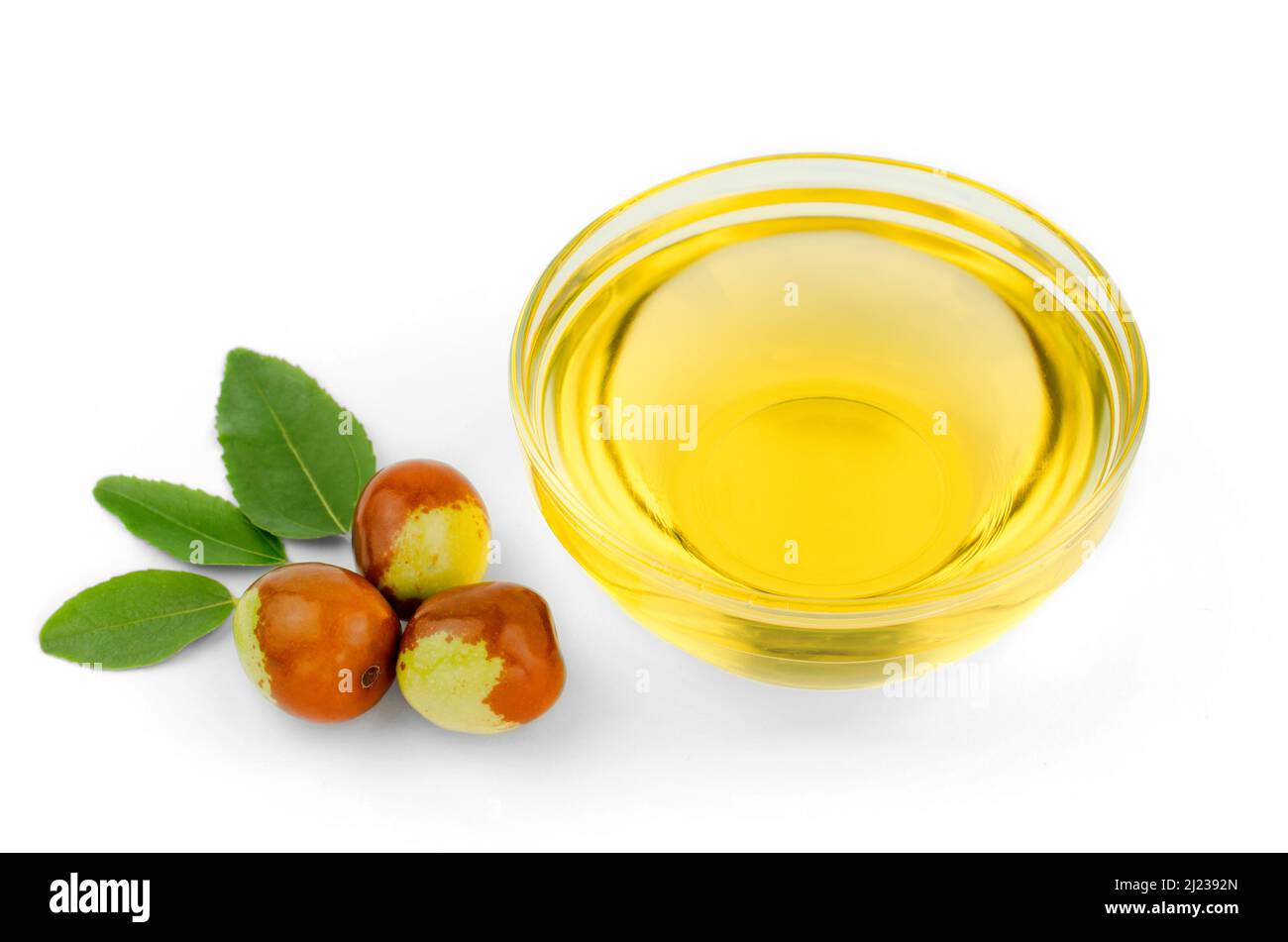 Bowl with jojoba oil, ripe fruits and green leaves on white background Stock Photo