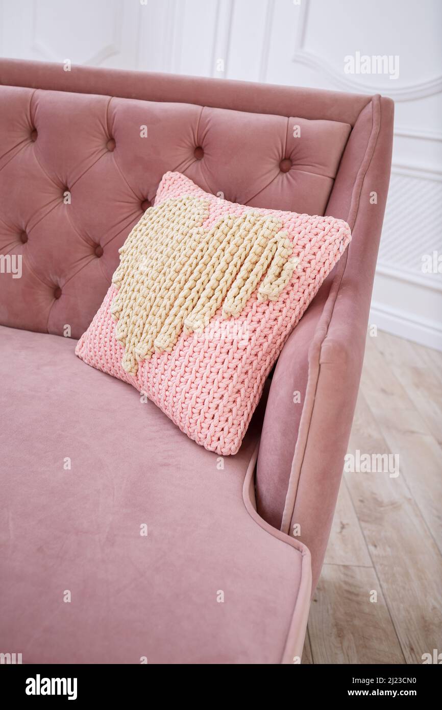 Knitted handmade pillow with pink threads lies on the sofa. Stock Photo