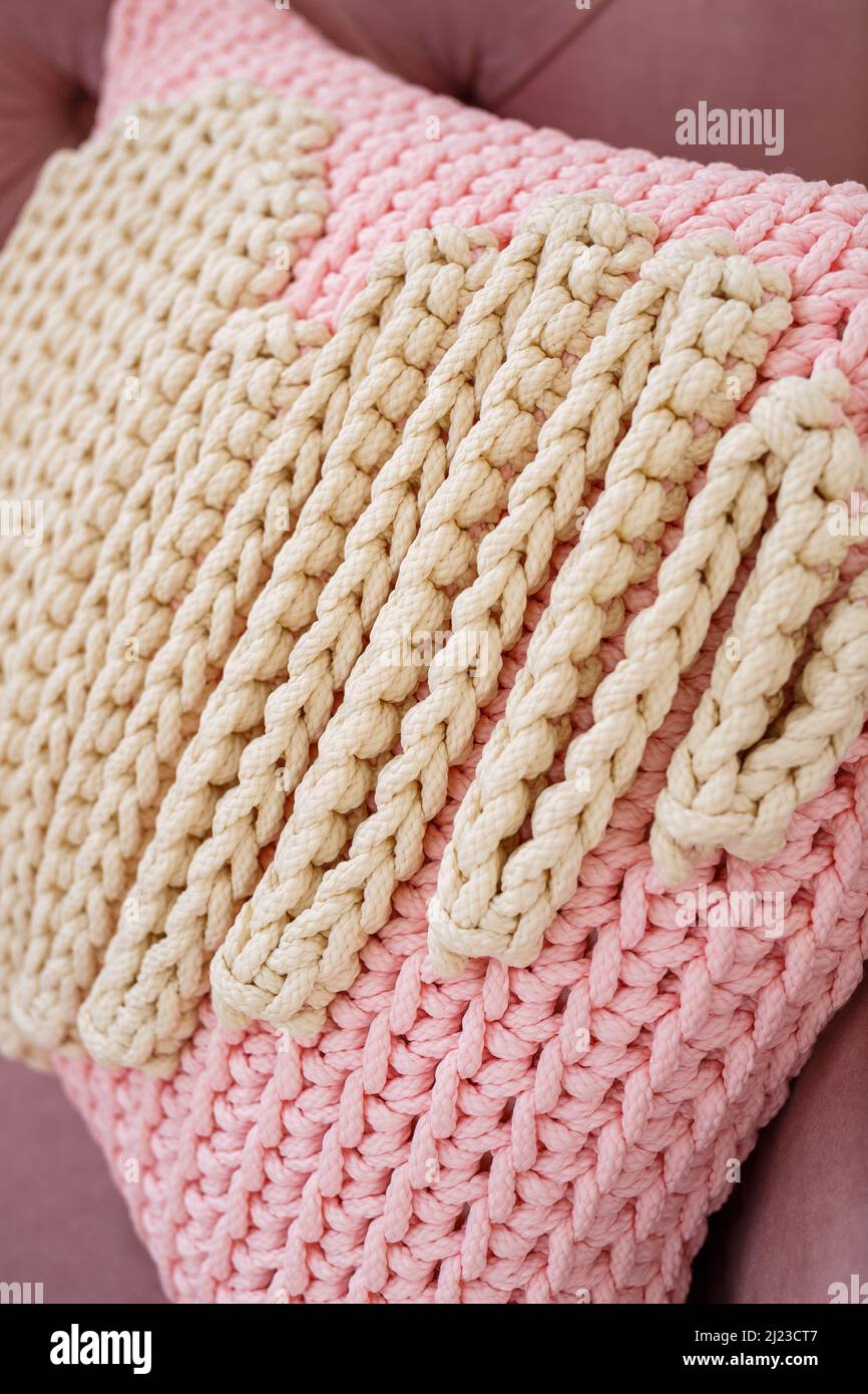 Knitted handmade pillow with pink threads lies on the sofa. Stock Photo