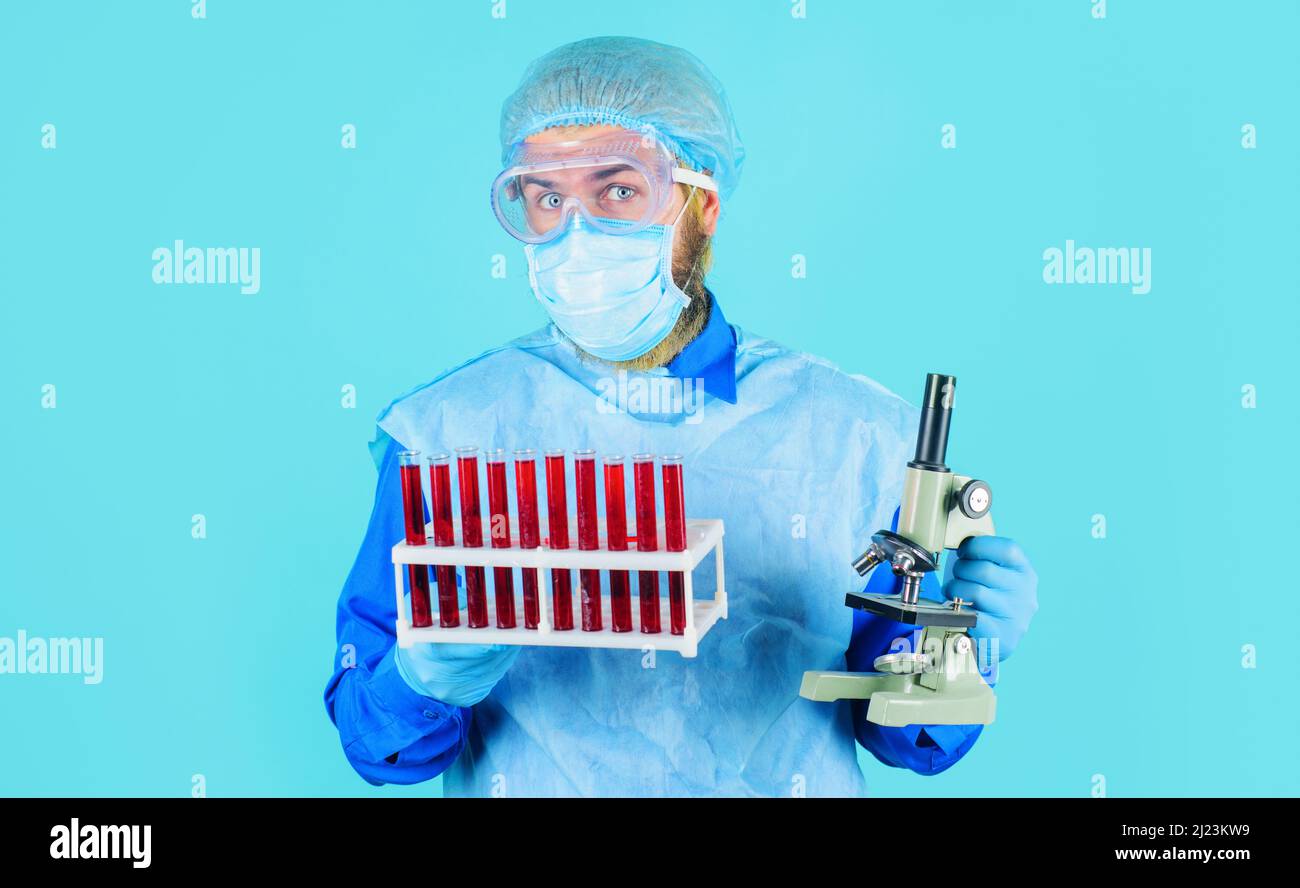 Doctor in protective suit, glasses and mask with blood sample tubes and microscope in laboratory. Stock Photo