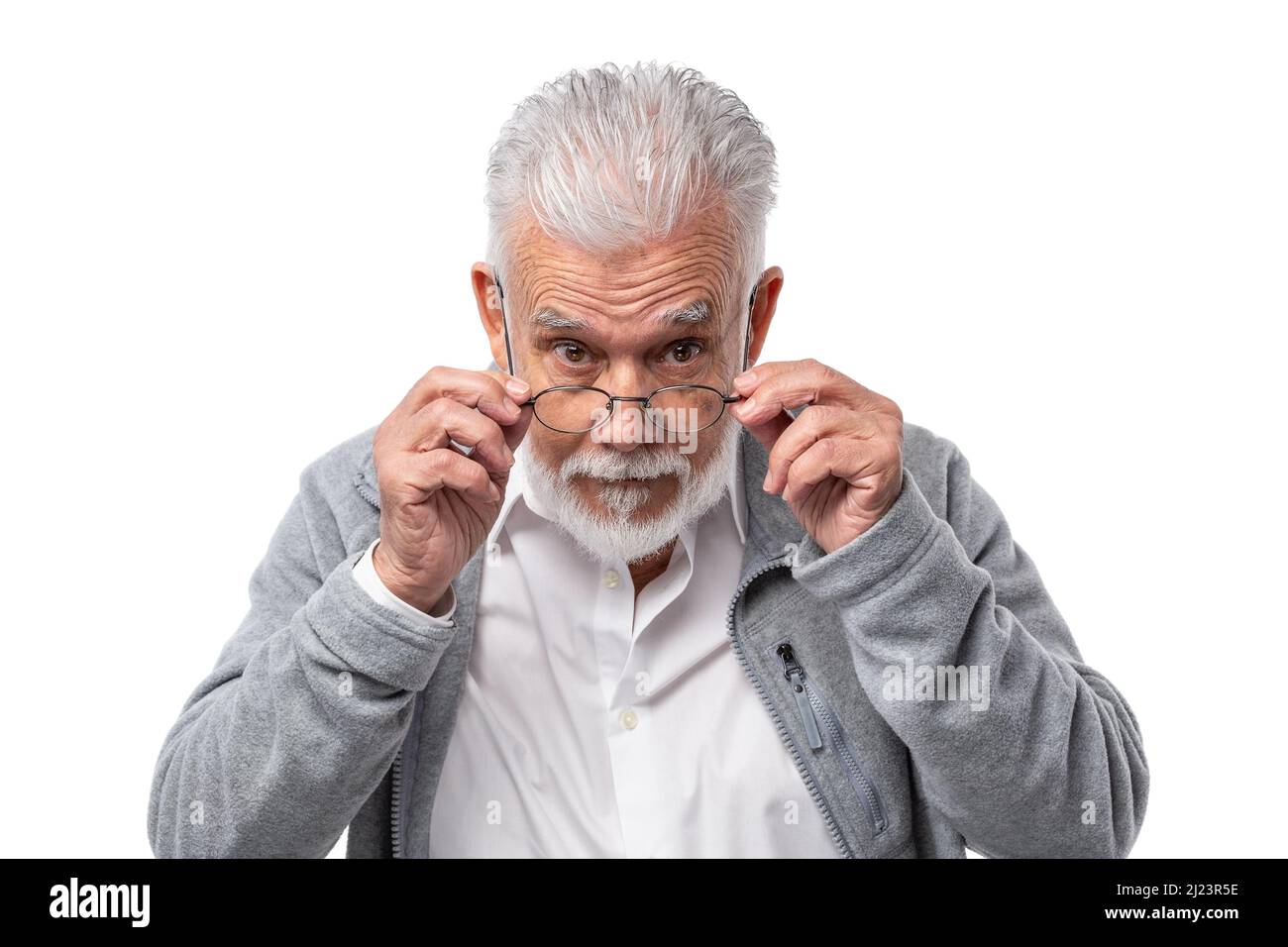 An elderly stylish man in glasses with a beard and gray hair looks from under forehead and holds glasses with his hands.  Stock Photo