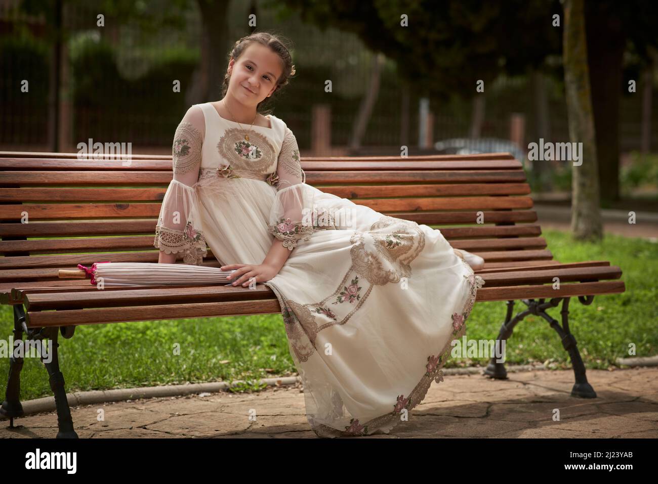 Communion girl posing sitting on a park bench Stock Photo