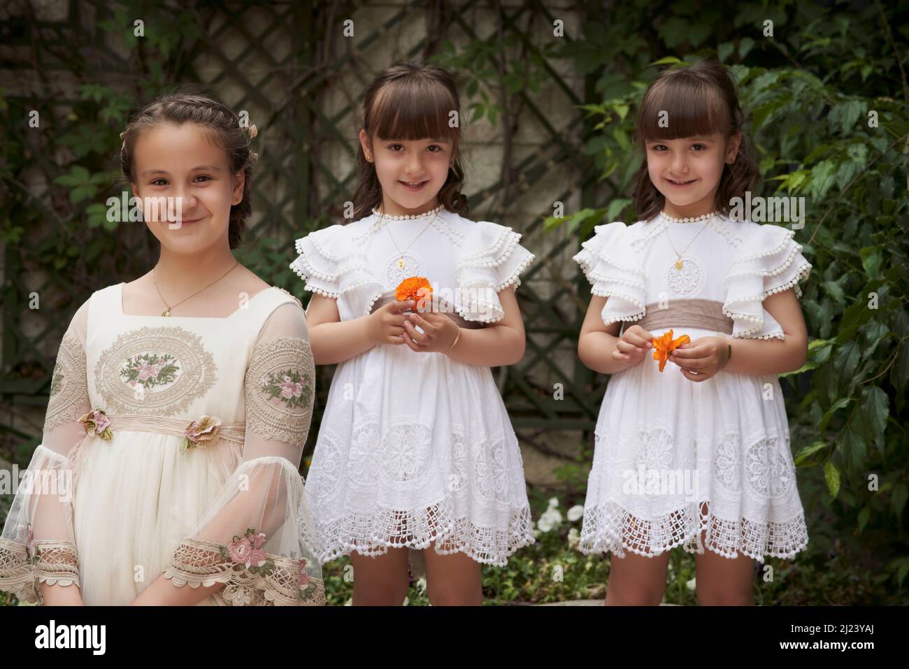 Communion girl posing with her twin little sisters in a park Stock Photo