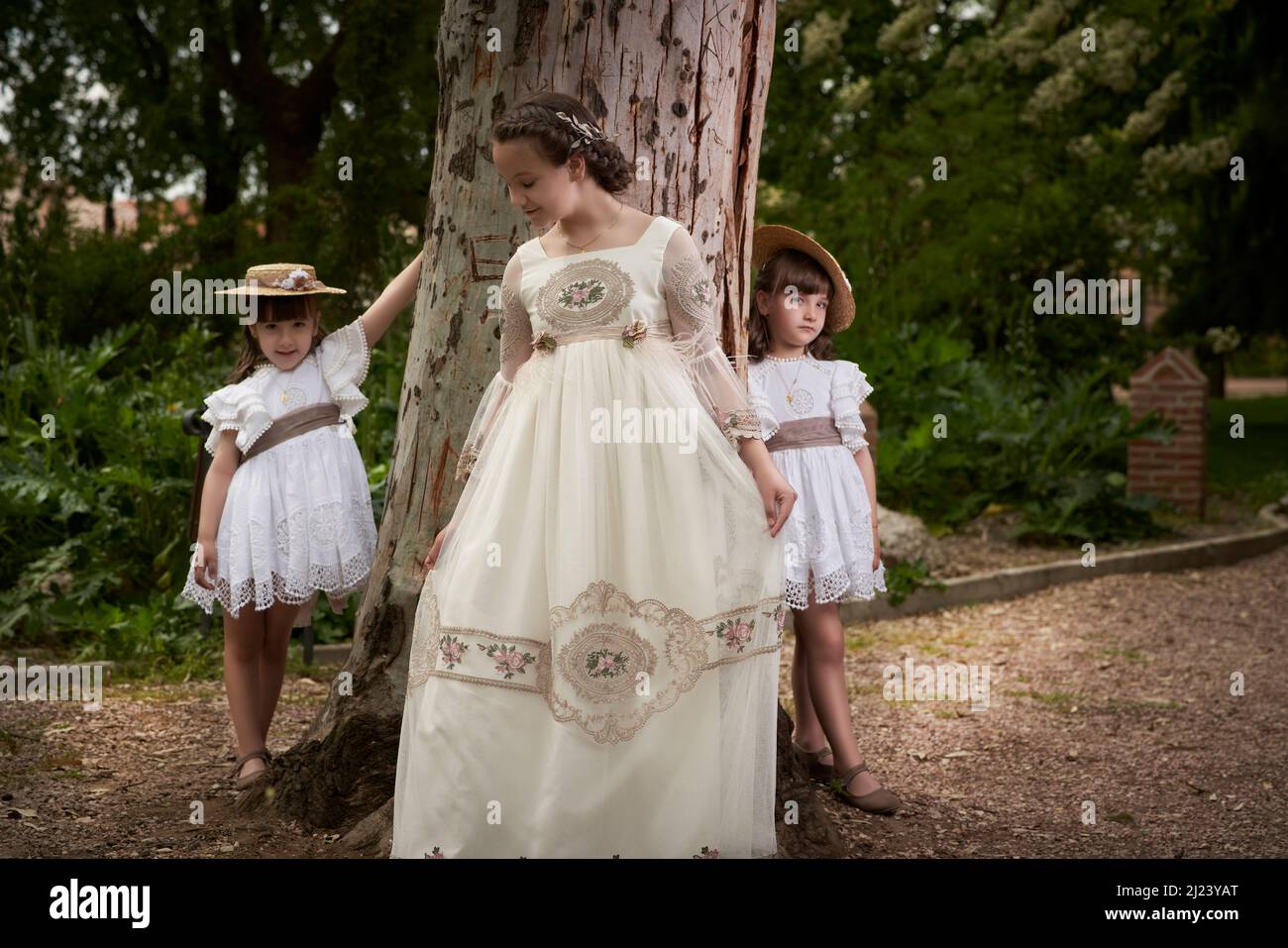 Communion girl posing with her twin little sisters in a park Stock Photo