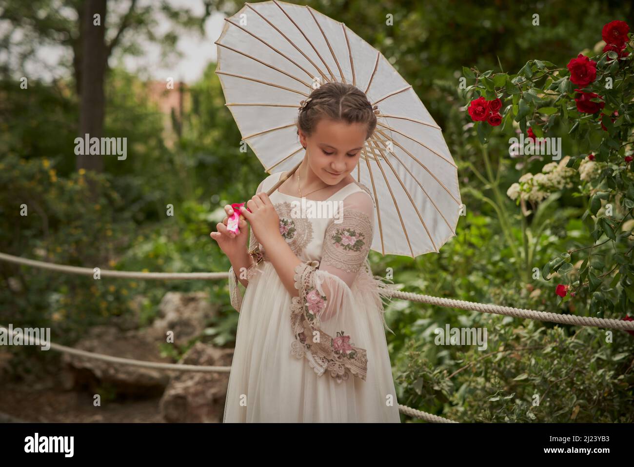 Communion girl posing with a white umbrella in a park Stock Photo