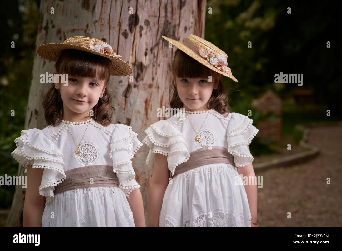 Communion twin little sisters next to a big tree in a park Stock Photo