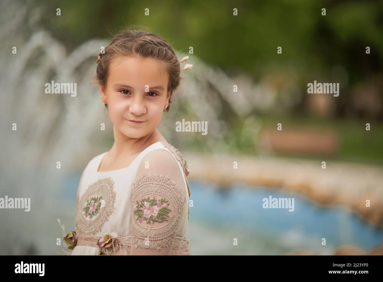 Communion girl posing in front of a fountain in a park Stock Photo