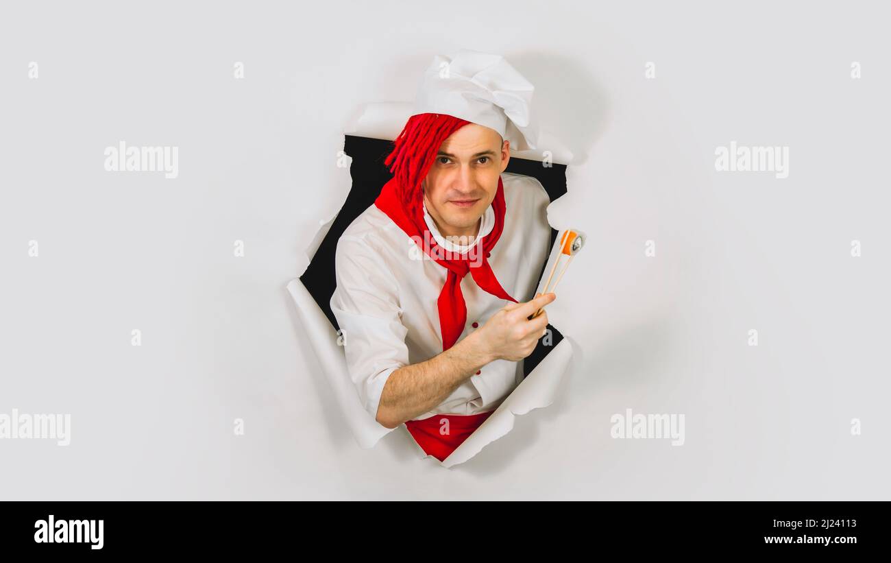 Young man dressed as chef holding chopsticks with roll. Male cook with