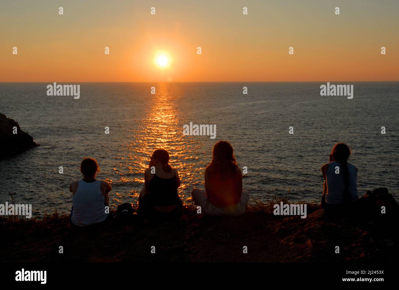 A group of friends gather to watch the sun set over the Pacific ocean in southern Mexico. Stock Photo