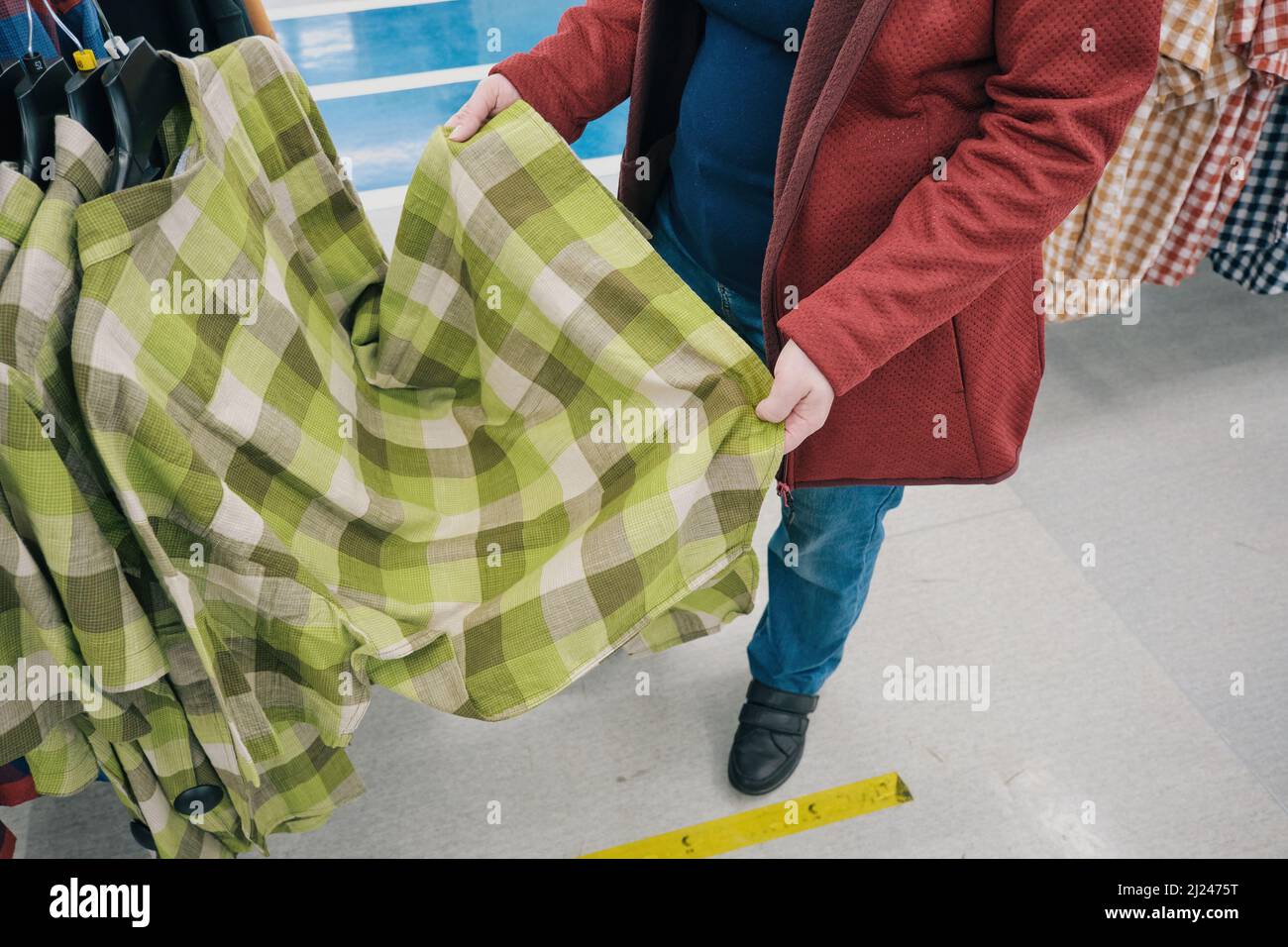 Pregnant woman chooses a roomy, green, flannelette plaid shirt in store to buy Stock Photo
