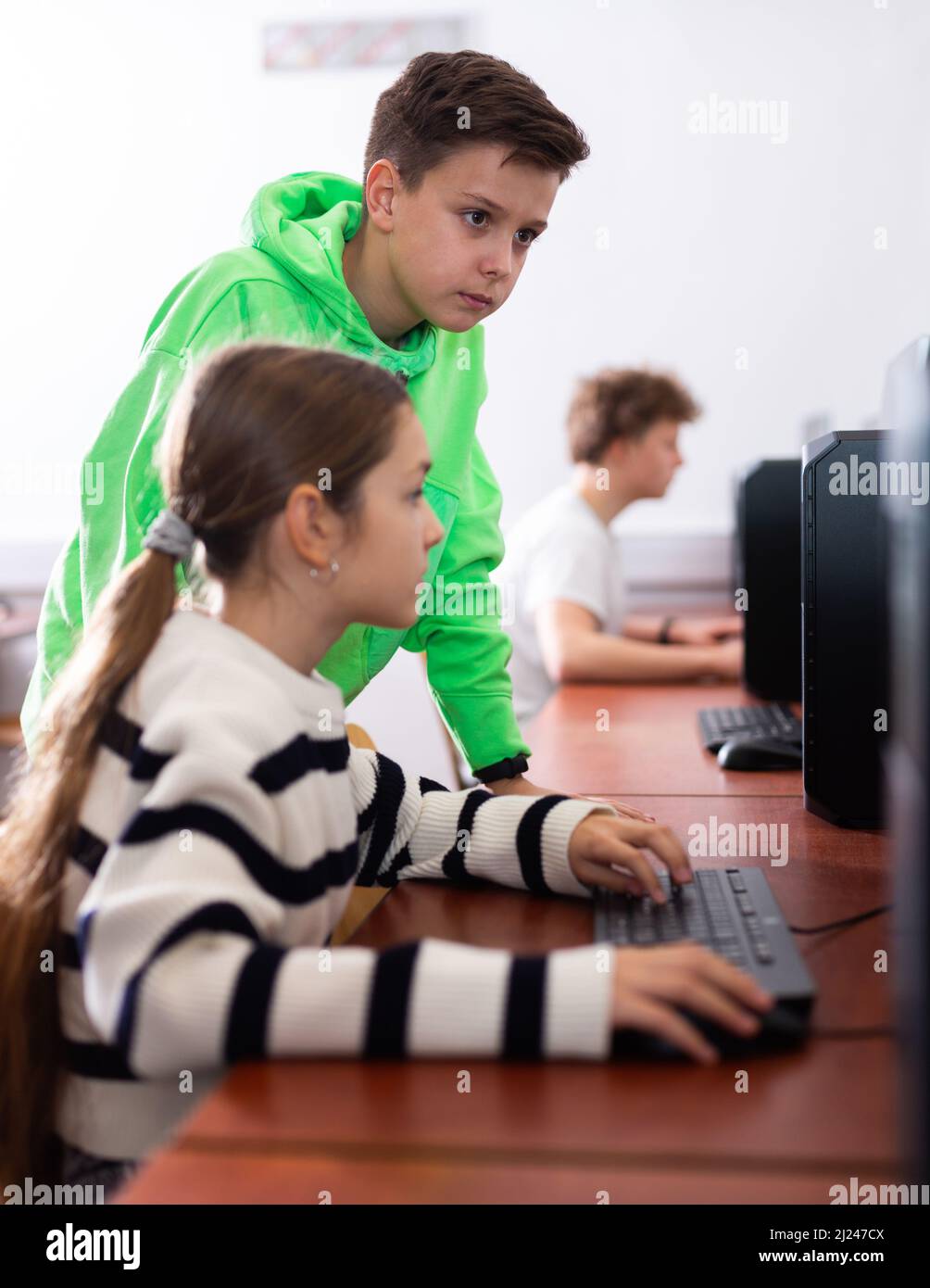 Preteen schoolboy helping girl classmate during informatics lesson ...