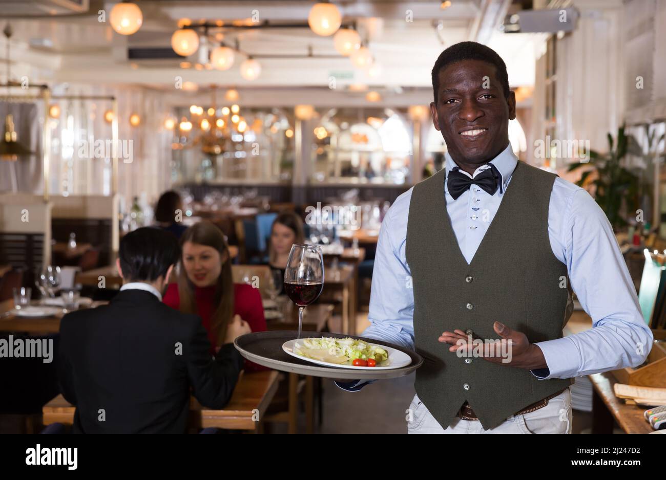 Nice waiter who is standing with order in hall Stock Photo - Alamy