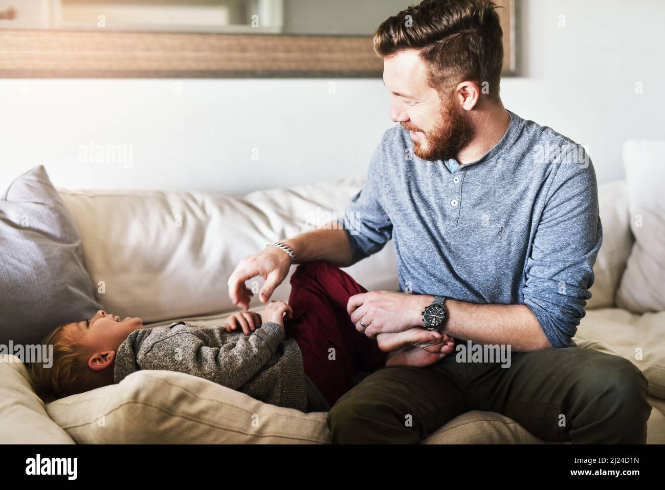 Tickle fight. Shot of a cheerful young man tickling his little boy while they hang out on the sofa at home during the day. Stock Photo